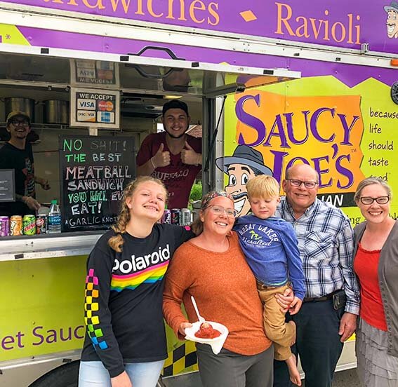 Happy family smiling with Saucy Joe's employees at home retirement party