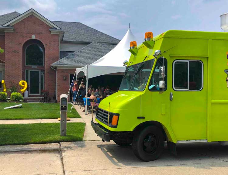 Green food truck parked and serving in front of home graduation party