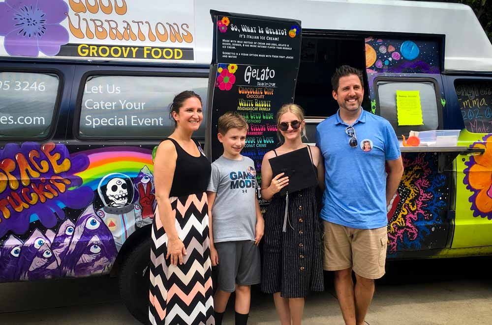 Graduate and family smiling in front of dessert truck at grad party