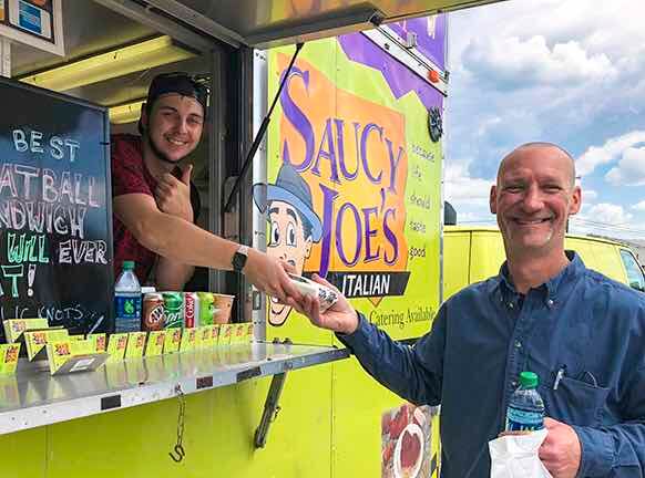 Food truck employee with thumbs up serving sandwich to happy customer