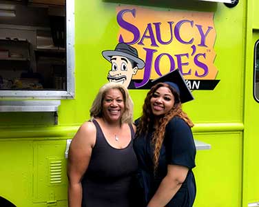 Mother and Daughter in Graduation cap and gown in front of food truck at grad party