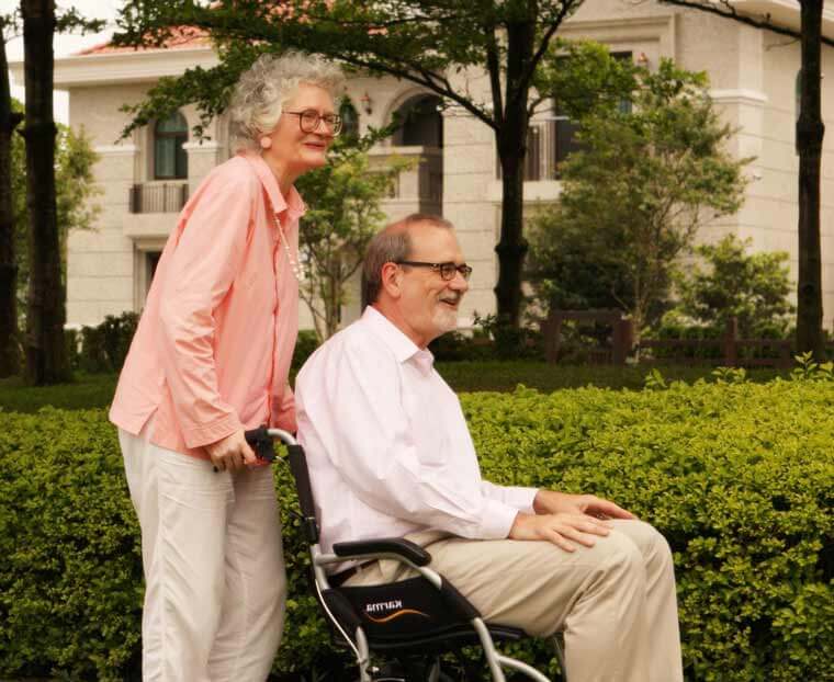 Elderly Woman Pushing Husbands Wheel Chair