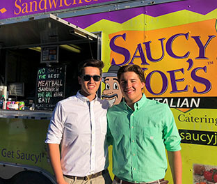 Two guys smiling at Saucy Joe's Food Truck at their graduation party