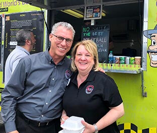 Smiling couple with food from Saucy Joe's at company picnic